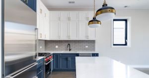 Discover the beautiful combination captured in this image of kitchen cabinets. The upper cabinets are presented in an elegant white tone, while the lower cabinets stand out in a bold navy blue. The white countertop adds a touch of brightness and contrast to the composition. The golden handles bring a sophisticated shine. This impressive color combination creates visually appealing contrast, infusing the kitchen with a sense of style and elegance. Enjoy the harmony between the white, navy blue, and the white countertop, enhanced by the golden details, in this captivating display of interior design.